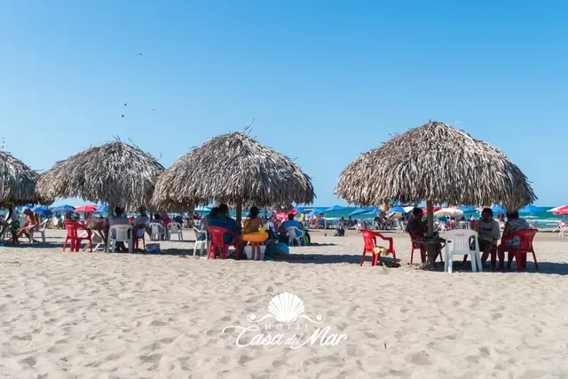 Palapas en la playa con mesas y sillas para los huéspedes · Hotel Casa del Mar